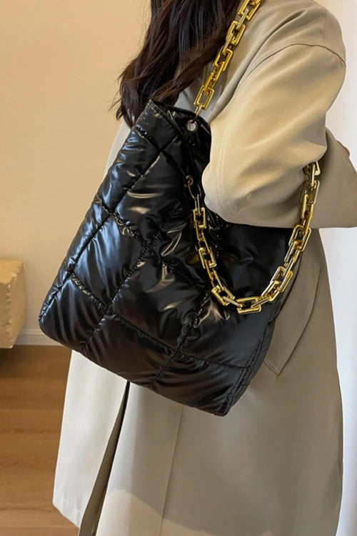 Model wearing a black quilted puffy handbag with a gold chain strap over her shoulder.